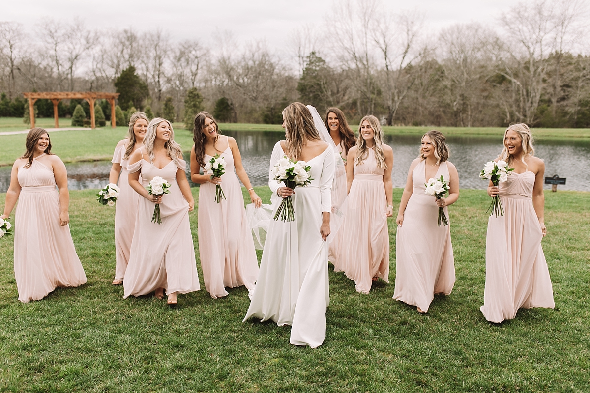 Bridesmaids wearing soft pink dresses and walking with bride outside
