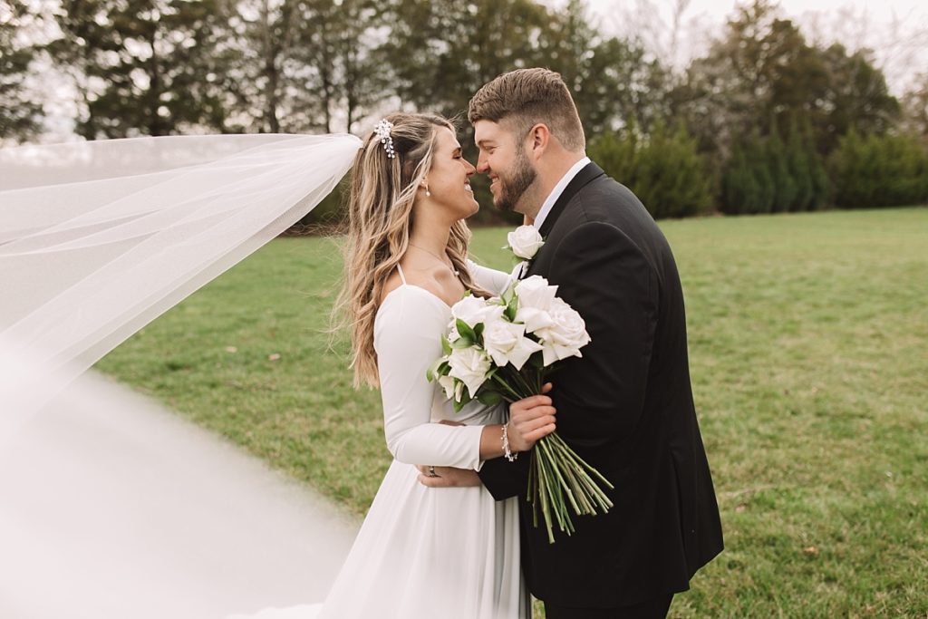 Cute photo of bride and groom nose to nose with veil flowing in the wind and white rose bouquet