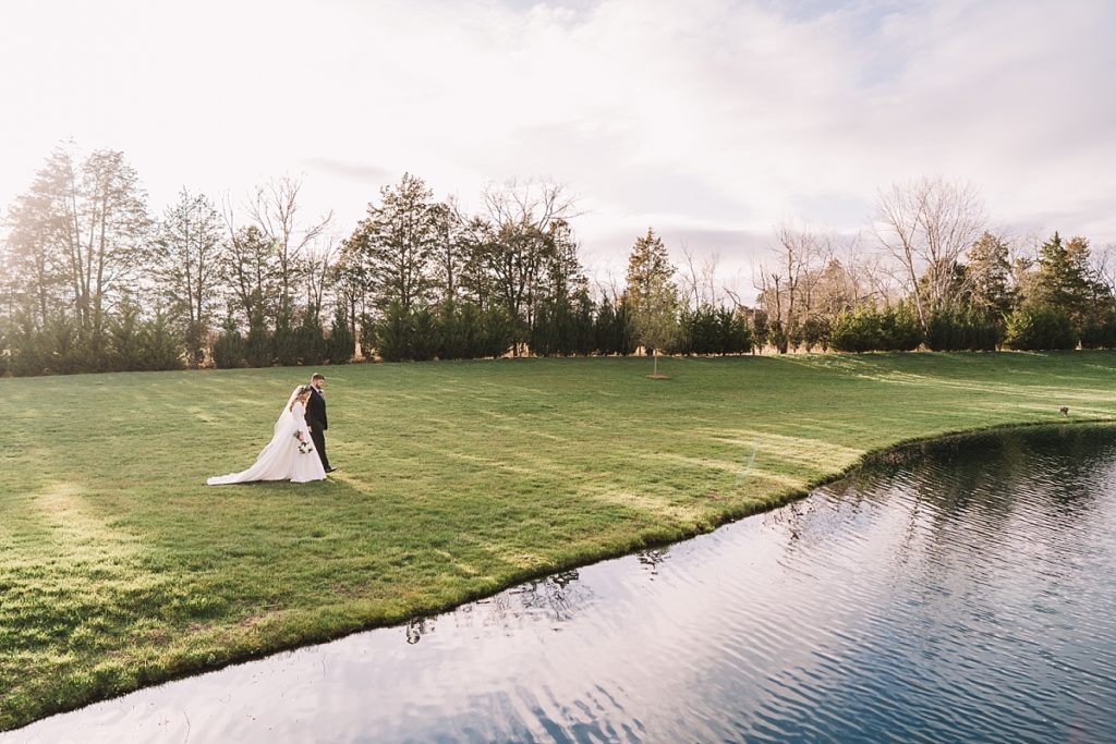 Dramatic landscape photo or bride and groom walking near the pond at The Barn at Sycamore Farms