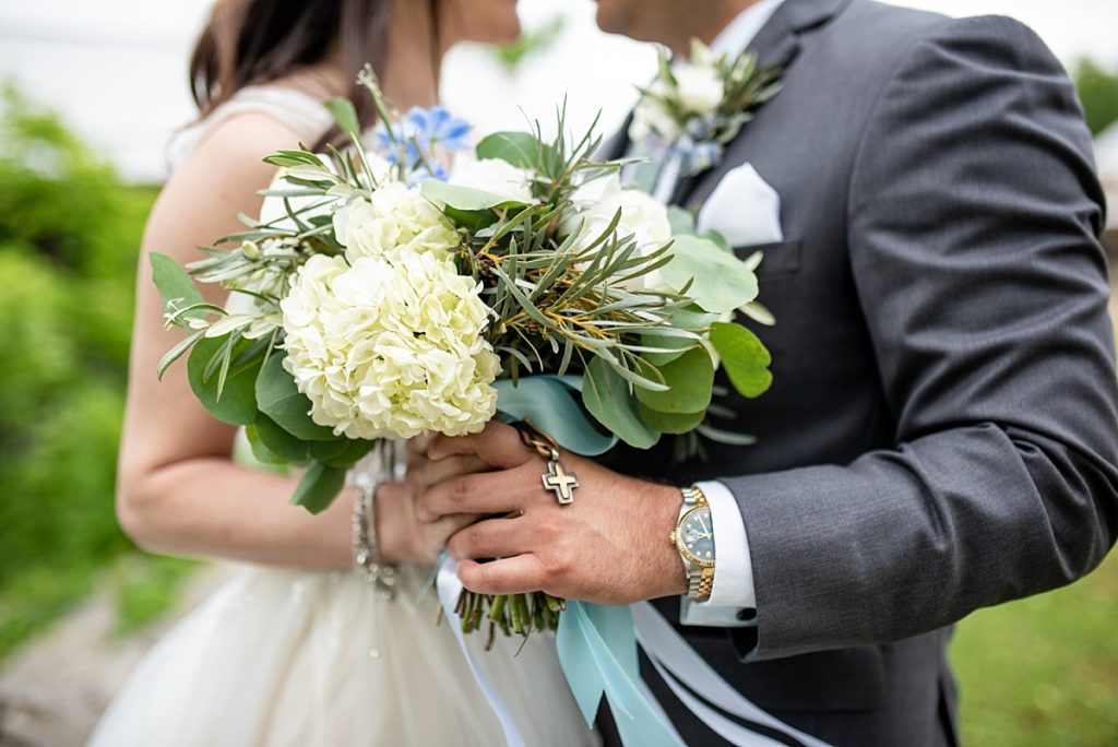 Detail photo of brides bouquet showing the greenery, hydrangeas, and rosary wrapped around the stem