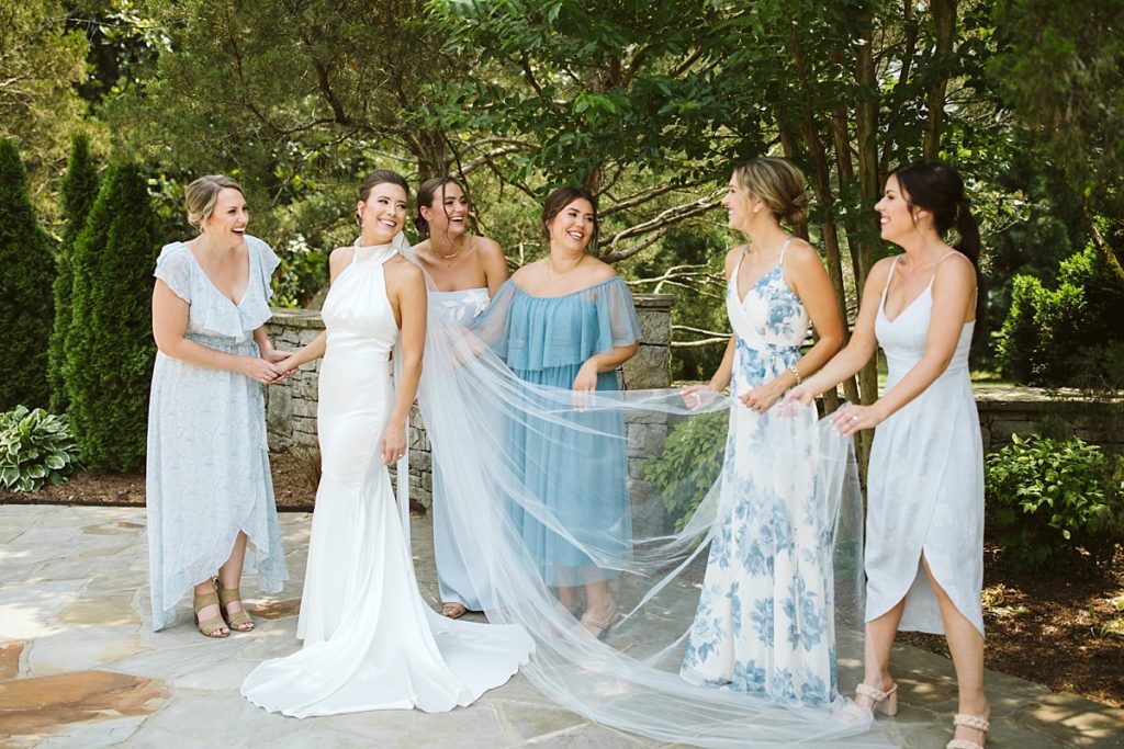 Bride smiling with her ladies while they play with her cathedral veil